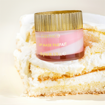 Catrice Lip Mask Parfait w różowo-białym słoiczku ze złotą zakrętką, leżący na kawałku kremowego tortu.