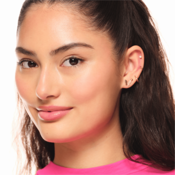 Portret młodej kobiety z długimi ciemnymi włosami, uśmiechem i kilkoma kolczykami w prawym uchu, widok z przodu.