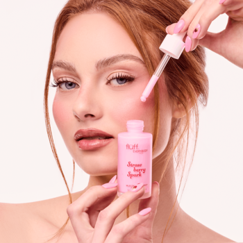 Kobieta z różowymi paznokciami aplikuje różowe mleczko do twarzy Fluff Strawberry Spark z brokatem, dla blasku.