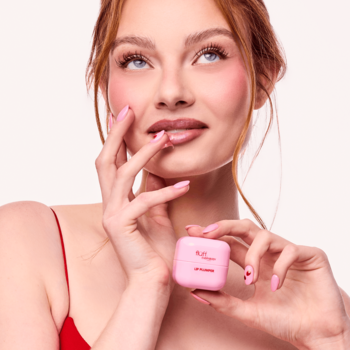 Kobieta trzyma różowy, kwadratowy Fluff Kiss Me Berry regenerujący lip plumper. Widoczne paznokcie w serduszka.