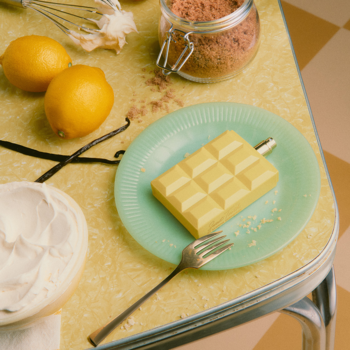 Sweet Tooth Lemon Pie perfumy. Żółta tabliczka na zielonym talerzu, wokół cytryny, wanilia i bita śmietana na żółtym blacie.