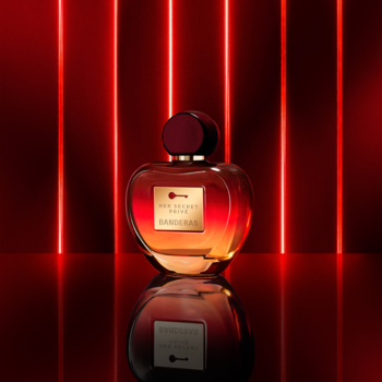 Perfum Bulgari Rose Goldea Blossom Delight. Zaokrąglona butelka, bursztynowy płyn, czerwony korek. Na tle czerwonych neonów.