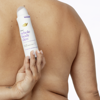 Biały dezodorant Dove Whole Body Deo Lavender & Chamomile, trzymany dłonią na tle nagich pleców.
