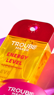 Zbliżenie na żółtą butelkę mgiełki Trouble Maker Energy Level Plumping Setting Mist z czerwoną nakrętką, pod kątem.