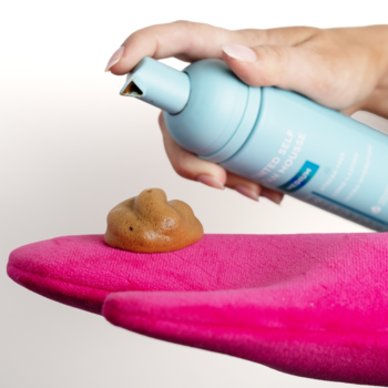 Pianka samoopalająca z niebieskiej butelki wyciskana na różową rękawicę do ciała. Zbliżenie na aplikację.