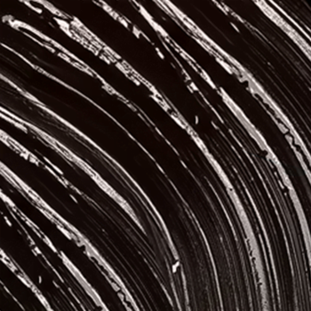 Makro czarnego tuszu L'Oreal Panorama z białymi, zakrzywionymi śladami po szczoteczce, podkreślające efekt objętości.