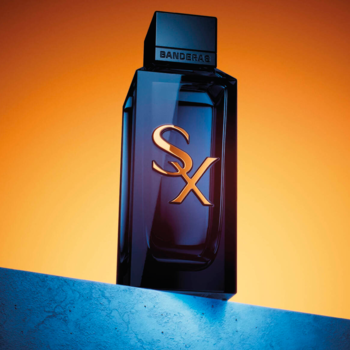 Prostokątne perfumy męskie Antonio Banderas SX, ciemnoniebieska butelka ze złotym logo, widok z przodu na tle pomarańczowo-niebieskim.