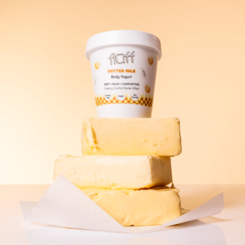 Fluff Butter Milk Body Yogurt w białym pojemniku na tle stosu trzech kostek masła; bogata, mleczna pielęgnacja.