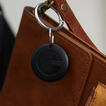 Czarny, okrągły smart lokalizator brelok w zbliżeniu, przypięty do paska brązowej torebki.