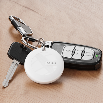 Biały, okrągły lokalizator kluczy Mili smart tag na metalowym breloczku z kluczykiem i pilotem, na drewnianym blacie.