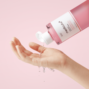 Różowy tonik medcube w przezroczystej butelce nalewany do dłoni na różowym tle, widoczne krople.