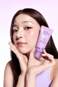 Młoda kobieta trzyma fioletowe serum SOMEBYMI Retinol Bakuchiol w tubce, blisko twarzy, na pastelowym tle.