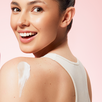 Uśmiechnięta kobieta z lśniącym beBIO mus do ciała tonic espresso na gładkim ramieniu, różowe tło.