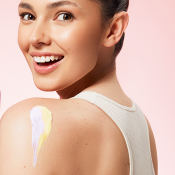 Kobieta uśmiecha się, prezentując dwuwarstwowy mus do ciała beBIO Honey & Fig w fioletowo-żółtych pasach na ramieniu.