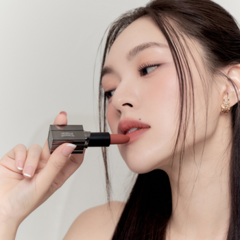 Kobieta z dłońmi blisko ust trzyma otwartą matową pomadkę Muzigae Mansion Prime nude.