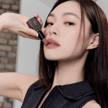 Zbliżenie na kobietę trzymającą matową pomadkę Muzigae Mansion Maxi w odcieniu nude przy ustach, soft blur.