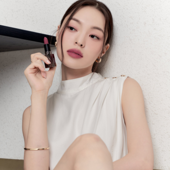 Modelka z matową pomadką Muzigae Mansion Hippy na ustach w odcieniu przydymionego różu, trzyma produkt.