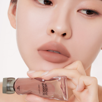 Kobieta z matowymi ustami w odcieniu nude trzyma lekki żelowy tint Muzigae Mansion Tension.