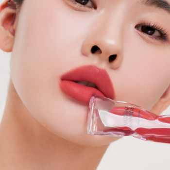 Muzigae Mansion lekki tint do ust Pleasure. Zbliżenie na usta z matowym, koralowym tintem i aplikatorem.