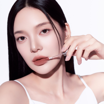 Zbliżenie na kobietę aplikującą lekki, matowy tint Muzigae Mansion Mania w odcieniu brązu na usta.