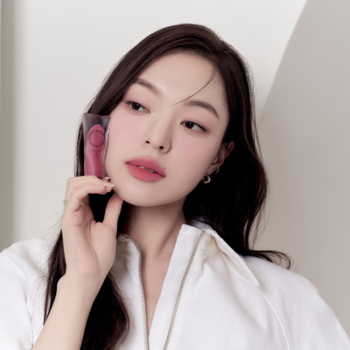 Kobieta, z różowymi matowymi ustami, w białej koszuli, trzyma tint Muzigae Mansion przy twarzy.