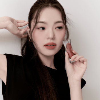 Kobieta prezentująca matowy tint do ust Muzigae Mansion Rare w szklanej buteleczce, widok z bliska na produkt.