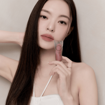 Kobieta trzyma matowy tint do ust Muzigae Mansion Pitch, zbliżenie na produkt i jej twarz.