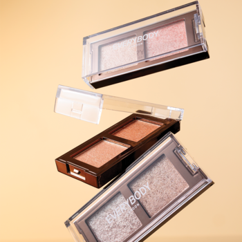 Trzy mini palety cieni Everybody London Retro Glam, metaliczne duo. Unoszą się na beżowym tle w przezroczystych opakowaniach.