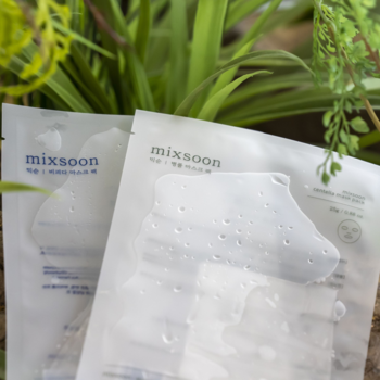 Dwie kojące maseczki mixsoon Centella Mask Pack w płachcie, białe z kroplami wody, na tle zielonych roślin.