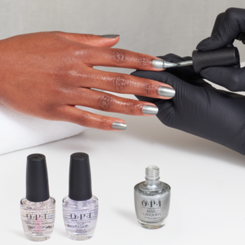 Manicure dłoni o ciemnej karnacji srebrnym, brokatowym lakierem OPI I'm Frosted. Z przodu trzy butelki OPI.