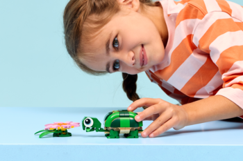 Uśmiechnięta dziewczynka bawi się zielonym żółwiem LEGO Creator 31377 z ruchomą głową i różową lilią.