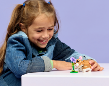 Uśmiechnięta dziewczynka bawi się LEGO Creator Uroczy chomik z kwiatkiem 31376 na białej powierzchni.