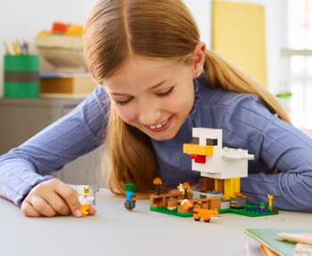 Dziewczynka buduje LEGO Minecraft Farma kurczaków 21585, uśmiechnięta, kurnik i figurki zwierząt.