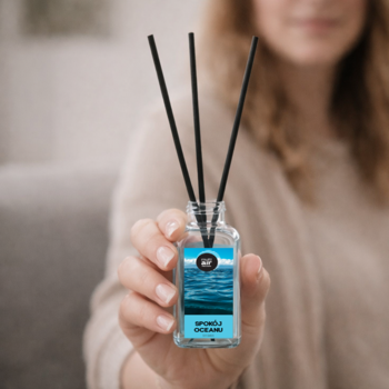Dyfuzor zapachowy "Zapach Oceanu" z czarnymi patyczkami, w szklanej butelce, trzymany w dłoni.
