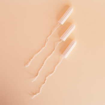 Trzy białe tampony Bestie Probiotyczne Medium z bawełnianymi sznurkami, ułożone ukośnie na jasnobrzoskwiniowym tle.