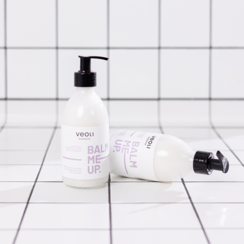 Dwie butelki balsamu Veoli Botanica Balm Me Up z czarnymi pompkami na białych kafelkach. Jedna stoi.