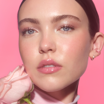 Kobieta z efektem dewy skin, makijażem w odcieniach różu, z różową różą, na jaskrawym tle.