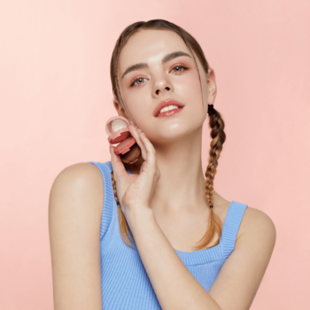 Młoda kobieta z Kaja Beauty Bento Coral Sunrise trio cieni do powiek przy policzku. Kompaktowe, warstwowe.