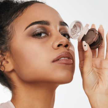 Kobieta z makijażem smoky eye trzyma otwarte trio cieni Kaja Beauty Bento Cold Brew, widoczne brązowe odcienie.