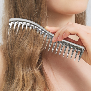 Srebrny grzebień ZURI Sister Young z szerokimi zębami czesze falowane włosy; zbliżenie dłoni.