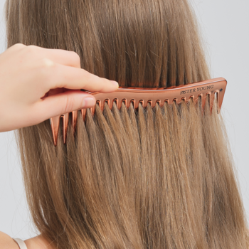 Ręka czesze długie, jasnobrązowe włosy różowo-złotym grzebieniem ZURI Sister Young z szerokimi zębami.