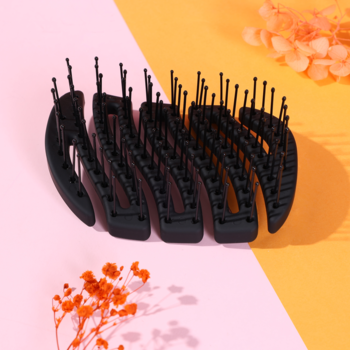 Czarna kompaktowa szczotka MILA Pocket Sister Young o falistej konstrukcji, elastyczne zęby, widok pod kątem na dwukolorowym tle.