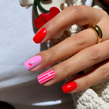 Dłoń z neonowym manicure Semilac 981 Spicy Neon. Paznokcie w intensywnej czerwieni i różu, z wisienkami i paskami.