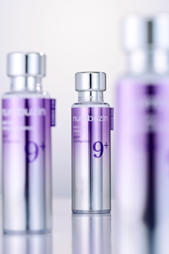 Liftingująca esencja numbuzin 9+ w srebrnej butelce z fioletową etykietą, fokus na centralnym opakowaniu.