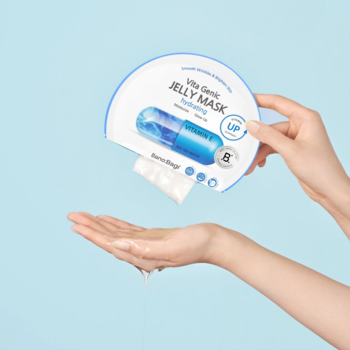 Ręka wyjmuje maskę Banobagi Vita Genic Jelly Mask Hydrating z opakowania na błękitnym tle, widok z przodu.