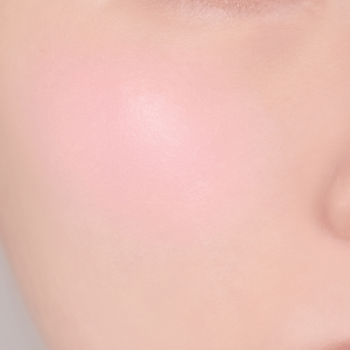 Zbliżenie na gładki policzek z subtelnym, jasnoróżowym rumieńcem. Makijaż z delikatnym różem do policzków.