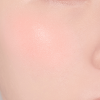 Zbliżenie na gładką skórę twarzy z delikatnym różowym rumieńcem na policzku, prezentujące efekt aplikacji różu.