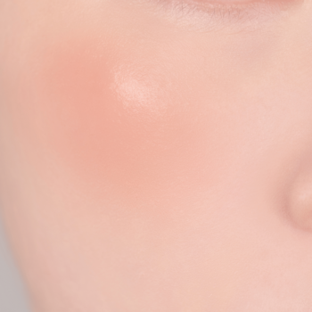 Zbliżenie na policzek z naturalnym różem w brzoskwiniowym odcieniu, dającym delikatne, matowe wykończenie.