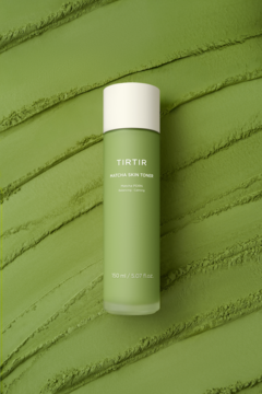 TIRTIR Matcha Skin Toner w matowej zielonej butelce z białą nakrętką na tle z pofalowanego proszku matcha. Widok z przodu.
