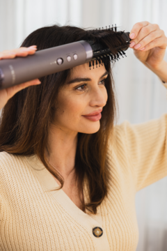 Kobieta używa szarej suszarko-lokówki Beautifly Flow Pro Styler do jednoczesnego suszenia i kręcenia włosów.